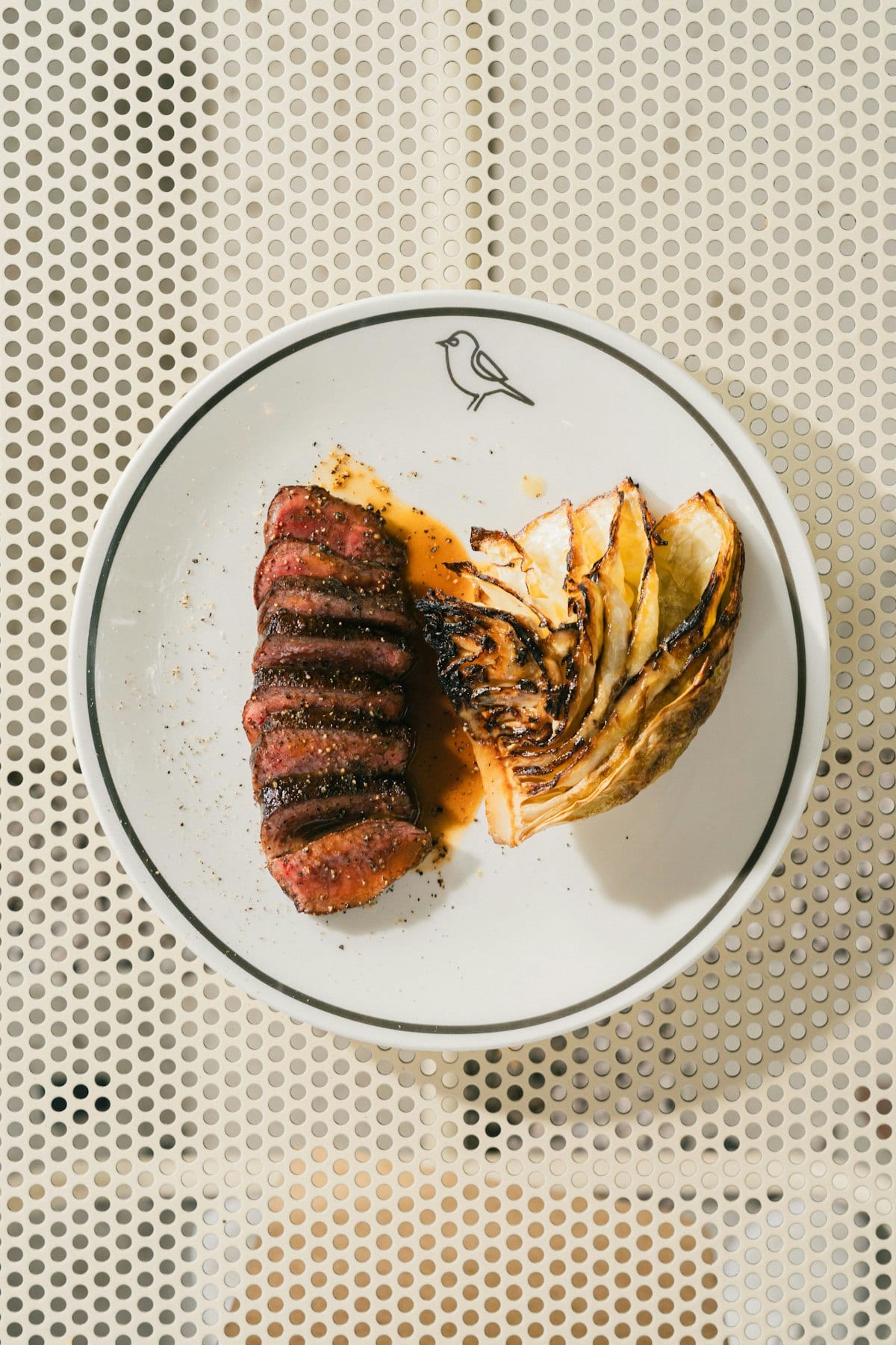Sliced steak with charred cabbage on a Birdie-branded plate.