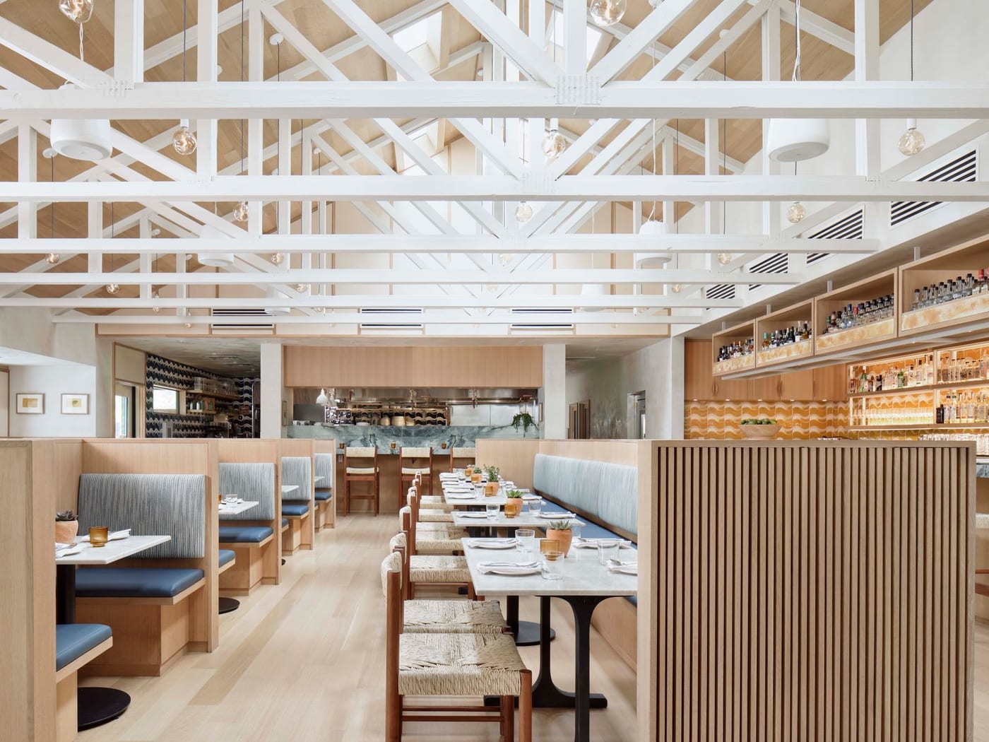 Bright Este dining room with white roof beams, blue booths, pale wood and open kitchen.