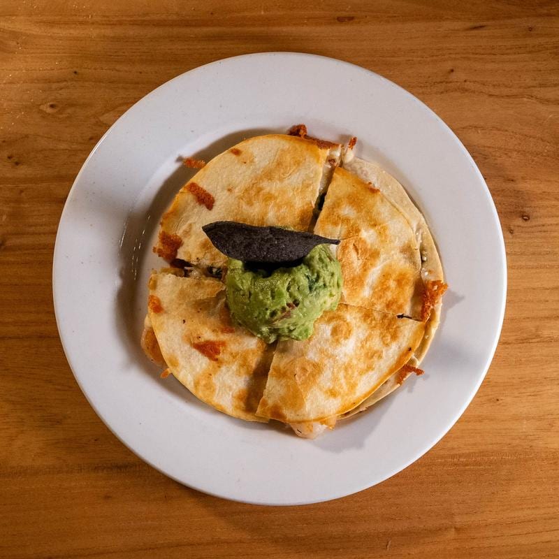 Plated dish with melted cheese, sauce and guacamole. Blue Corn Harvest.