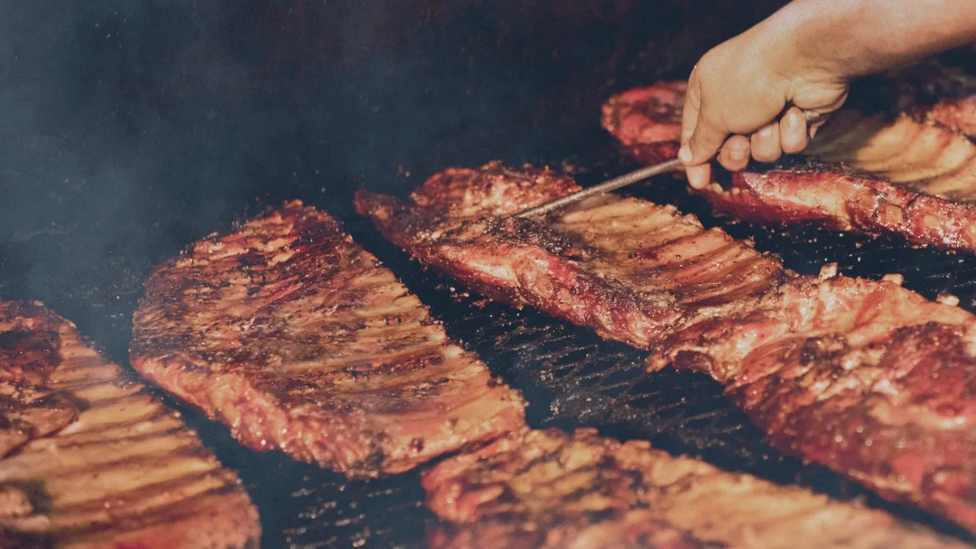 Hands slicing barbecue over a wood-fired pit. Kreuz Market.